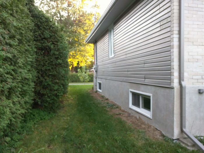 Spraying polyurethane over pink foam board on exterior wall under vinyl