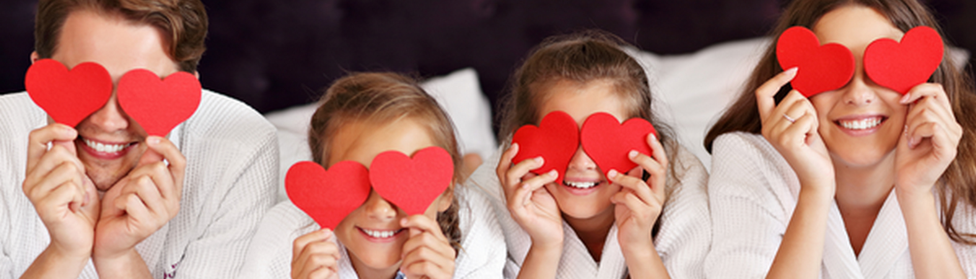 Family of four on a hotel bed holding paper hearts