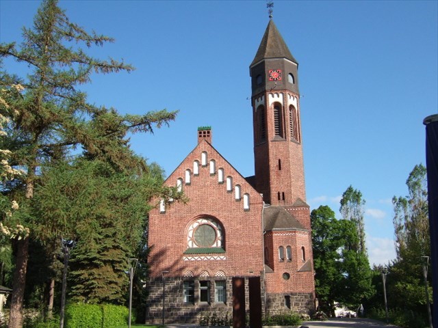 Backstein-Gebäude der Hephata-Kirche mit Kirchturm und dem rostfarbenen Mahnmal im Vordergrund