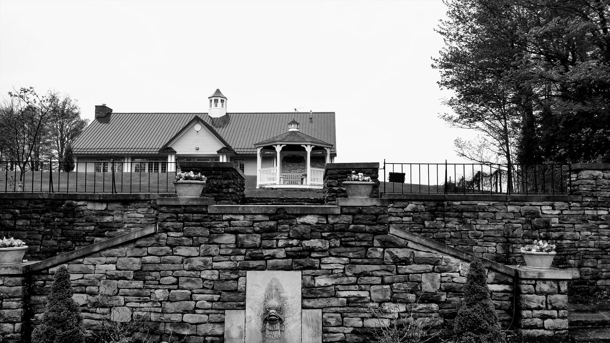 Black and white image of small octagonal gazebo in the foreground, and a much larger pavilion in the background