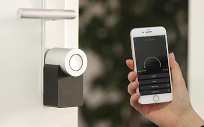 A person holds up a smartphone to a smart keyless entry lock on a door.