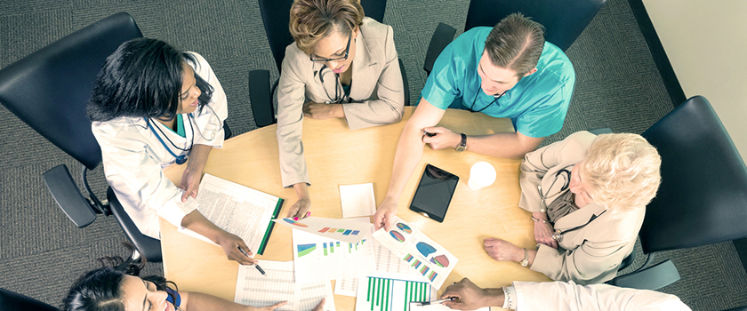 A group of medical professionals is seated at a table discussing handouts with charts, graphs and tables.