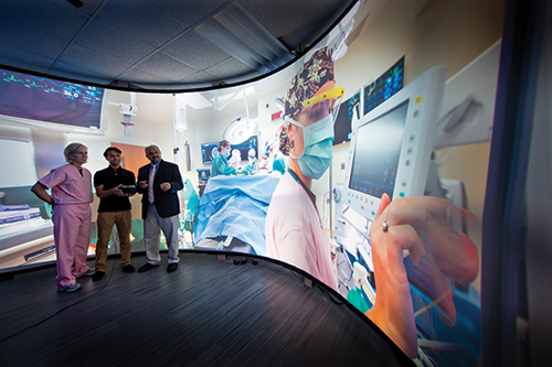 AR/VR in the IR Suite hero image Three individuals looking at giant screen with video of procedure