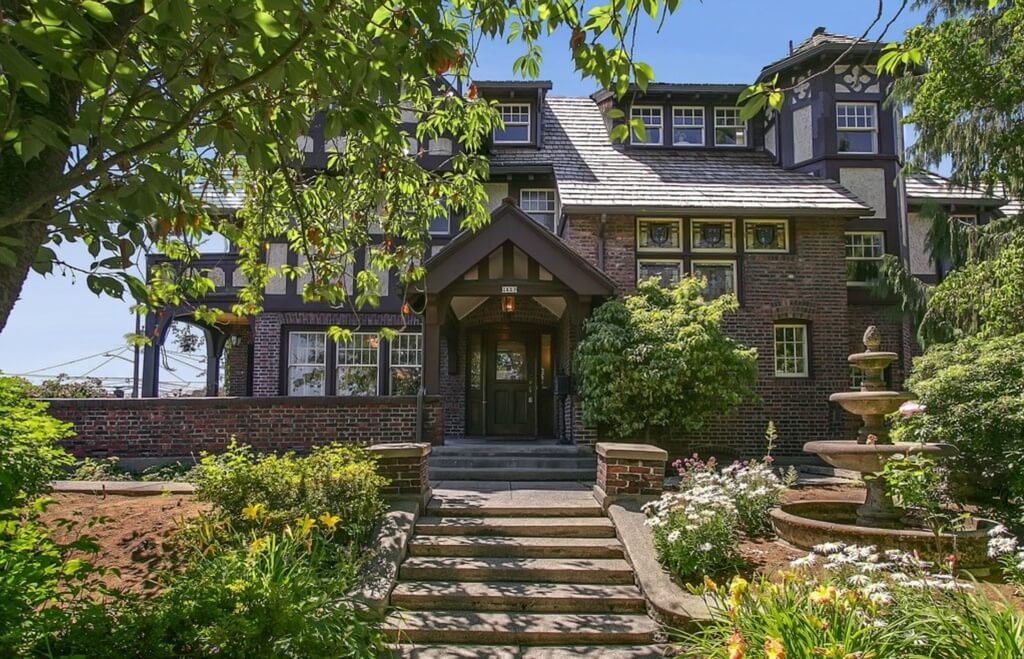Here is the Hainsworth mansion as seen walking up the front entrance. Concrete stairs elevate to a wraparound path before reaching the brick walled patio and main entryway. Sloped garden with large fountain flanks the stairs. Here is the Hainsworth mansion as seen walking up the front entrance. Concrete stairs elevate to a wraparound path before reaching the brick walled patio and main entryway. Sloped garden with large fountain flanks the stairs.