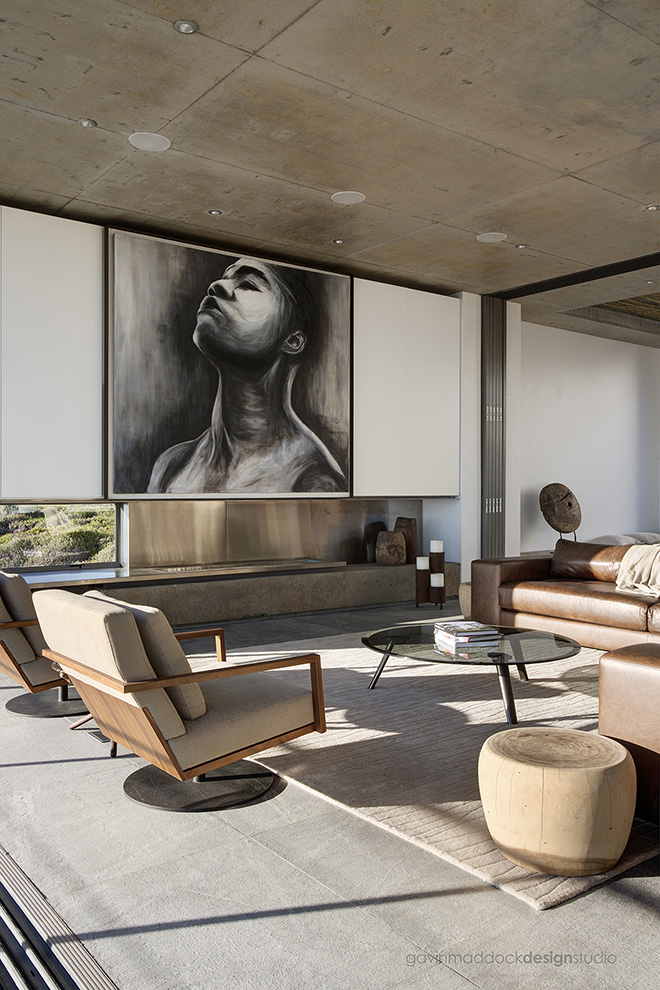 Large art piece towers over the living room, with sand toned area rug defining the space. Contemporary brown leather sectional joins a pair of modern wood and fabric swivel chairs around a modern glass coffee table. Large art piece towers over the living room, with sand toned area rug defining the space. Contemporary brown leather sectional joins a pair of modern wood and fabric swivel chairs around a modern glass coffee table.