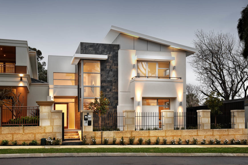 The front facade, as seen from street side, folds multiple textures and layers of glass into one view, set back behind a low slung brick and wrought iron fence. Two story window in stone clad corner showcases the large central staircase. The front facade, as seen from street side, folds multiple textures and layers of glass into one view, set back behind a low slung brick and wrought iron fence. Two story window in stone clad corner showcases the large central staircase.