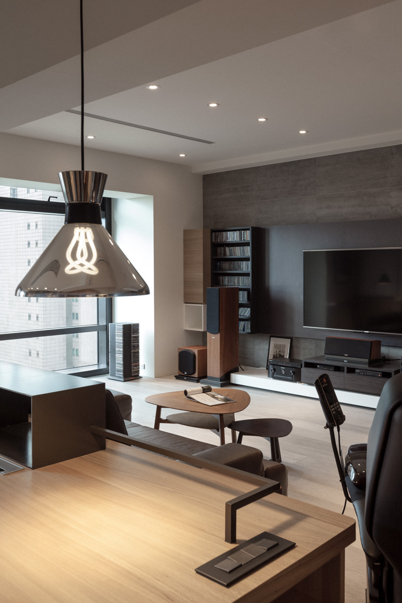 The space is awash in neutral, natural tones, from light hardwood flooring, to white walls and grey media backdrop. Floor to ceiling windows at left provide ample natural light. The space is awash in neutral, natural tones, from light hardwood flooring, to white walls and grey media backdrop. Floor to ceiling windows at left provide ample natural light.