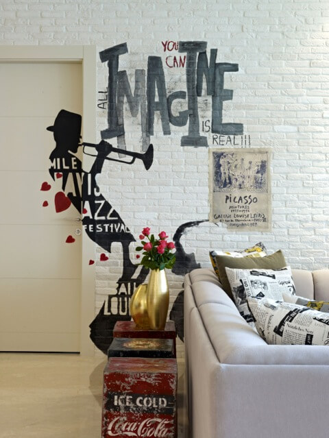 The white brick walls hold numerous detailed personal touches, like this Miles Davis "graffiti" and Picasso art print. The lush white sofa is populated with newsprint style throw pillows. The white brick walls hold numerous detailed personal touches, like this Miles Davis "graffiti" and Picasso art print. The lush white sofa is populated with newsprint style throw pillows.