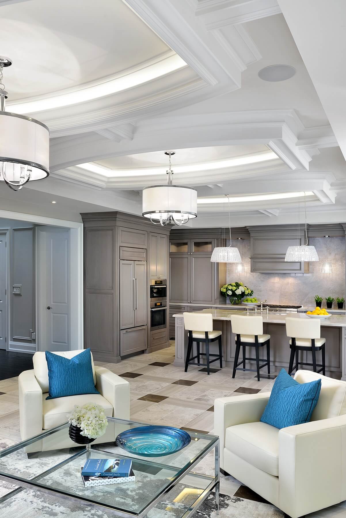 Central open space shares living room and kitchen, with an expanse of tile flooring pairing various shades of marble into an intricate pattern. White leather armchairs hold flashes of bold blue amidst the neutral theme. Central open space shares living room and kitchen, with an expanse of tile flooring pairing various shades of marble into an intricate pattern. White leather armchairs hold flashes of bold blue amidst the neutral theme.