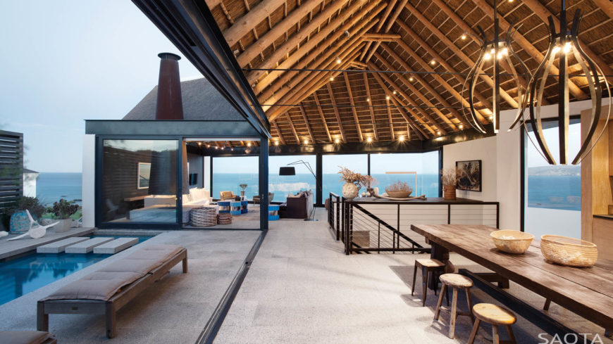 Viewed in the opposite direction, we see how the fully open design of the main floor spills from the kitchen into a dining and living room area, with the conical flue seen at left. Vaulted ceilings of natural exposed beams hold embedded lighting throughout. Viewed in the opposite direction, we see how the fully open design of the main floor spills from the kitchen into a dining and living room area, with the conical flue seen at left. Vaulted ceilings of natural exposed beams hold embedded lighting throughout.
