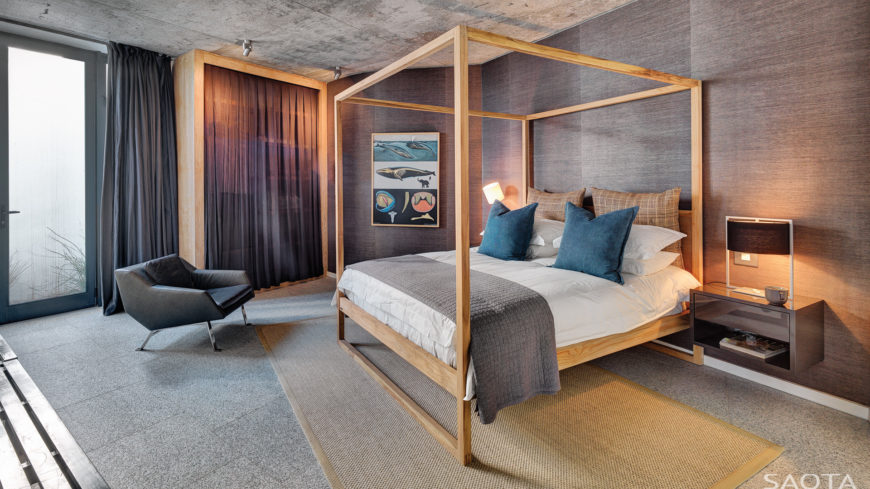 This master bedroom features a canopy bed with a floating nightstand and accent chair. It sits on a beige rug over carpet flooring.