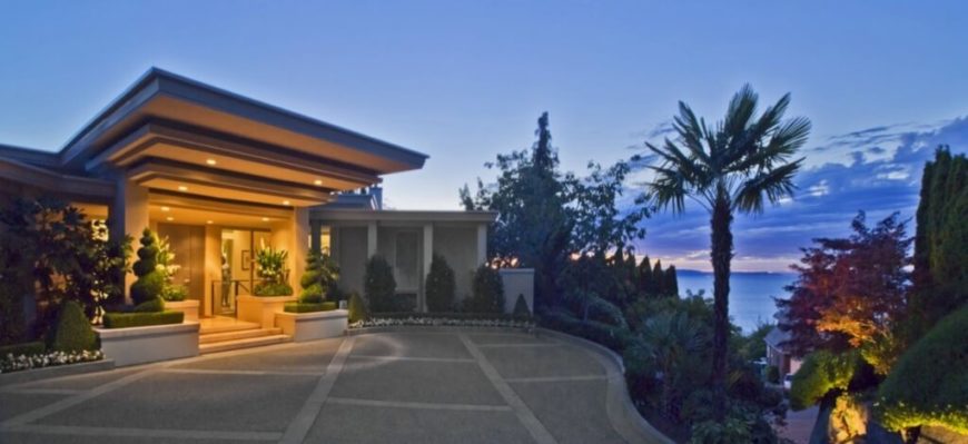 Approaching the home from the drive, a cornucopia of landscaping wraps the sharply defined modern structure. A large, illuminated overhang dominates the entrance. Approaching the home from the drive, a cornucopia of landscaping wraps the sharply defined modern structure. A large, illuminated overhang dominates the entrance.
