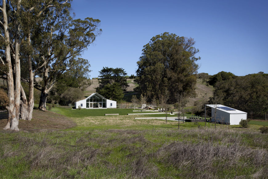 This wide view of the ranch puts the barn house and accompanying pool house into context, revealing the gently hilly landscape within which it fits. The angular white structure's facade is dominated by glass panels for a transparent look. This wide view of the ranch puts the barn house and accompanying pool house into context, revealing the gently hilly landscape within which it fits. The angular white structure's facade is dominated by glass panels for a transparent look.