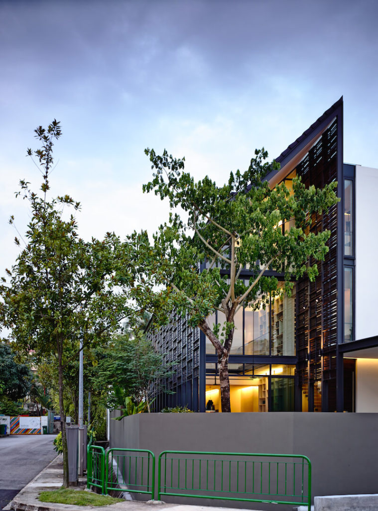 An exterior shot from the street corner, showing the multiple railings and fences around the home. Lush landscaping and trees peek out from behind the concrete wall. An exterior shot from the street corner, showing the multiple railings and fences around the home. Lush landscaping and trees peek out from behind the concrete wall.