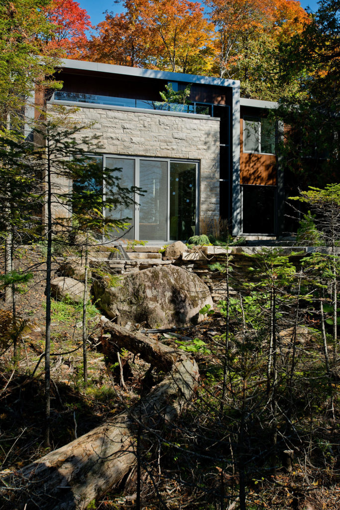 Here we see the home from the lake side, surrounded by large stones and forest, rising out of the environment. Here we see the home from the lake side, surrounded by large stones and forest, rising out of the environment.