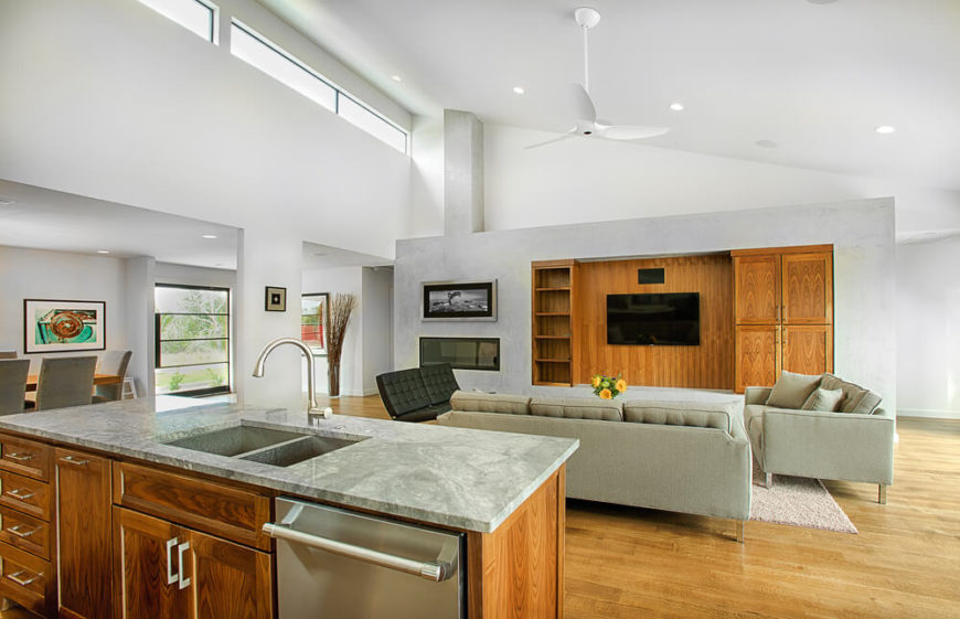 The open-plan design creates an immense central open space, with living, dining, and kitchen areas centered beneath a two story angled ceiling. The marble topped island overlooks a set of contemporary sofas and large entertainment wall featuring shelving and built-in fireplace. The open-plan design creates an immense central open space, with living, dining, and kitchen areas centered beneath a two story angled ceiling. The marble topped island overlooks a set of contemporary sofas and large entertainment wall featuring shelving and built-in fireplace.