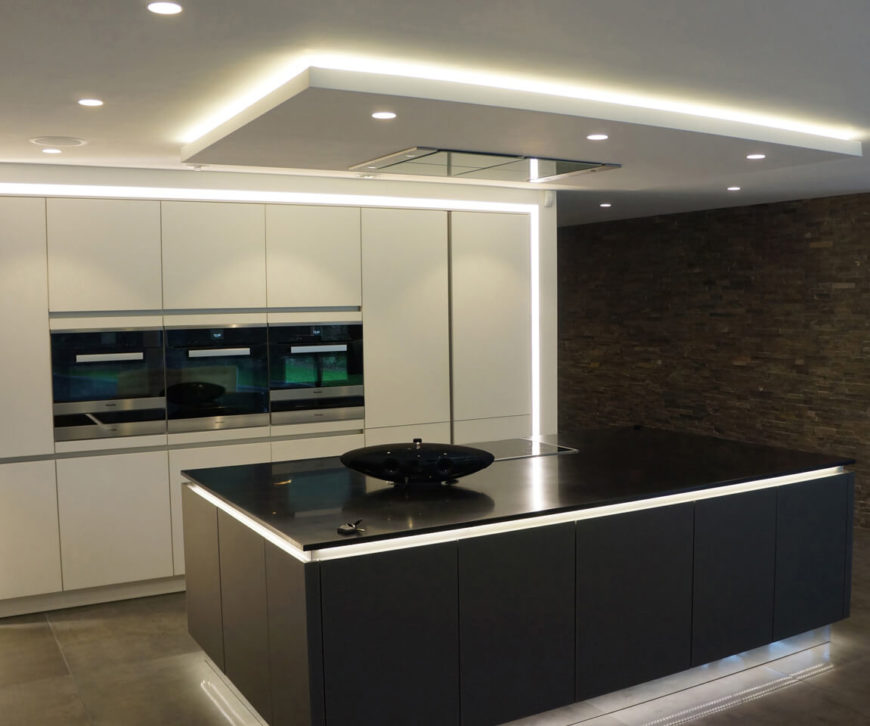 Moving inside, we first visit the kitchen, centering on an immense black island that "floats" over the floor, courtesy of intricately placed lighting. Built-in strips of light on the lower and upper edges create a unique counterpoint to the sleek white cabinetry of the room. Moving inside, we first visit the kitchen, centering on an immense black island that "floats" over the floor, courtesy of intricately placed lighting. Built-in strips of light on the lower and upper edges create a unique counterpoint to the sleek white cabinetry of the room.