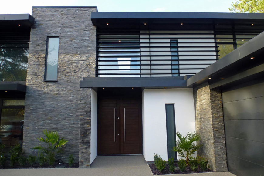 The front entrance is set back into the home, with rich dark wood doors and sleek metal hardware. The textural brick exterior complements splashes of white and black metal. The front entrance is set back into the home, with rich dark wood doors and sleek metal hardware. The textural brick exterior complements splashes of white and black metal.