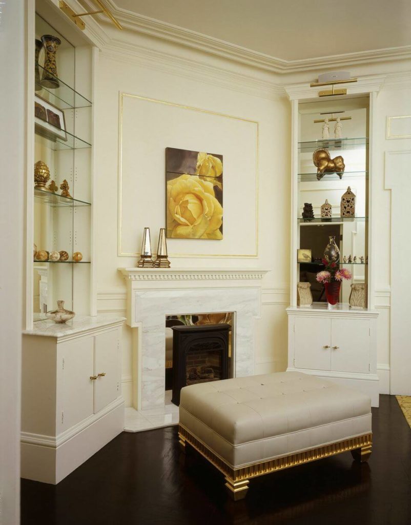 The white marble fireplace of the study is flanked by two small built-in cabinets topped by mirrors. A large white leather ottoman with golden supports contrasts with the luxurious dark wood floors. The white marble fireplace of the study is flanked by two small built-in cabinets topped by mirrors. A large white leather ottoman with golden supports contrasts with the luxurious dark wood floors.