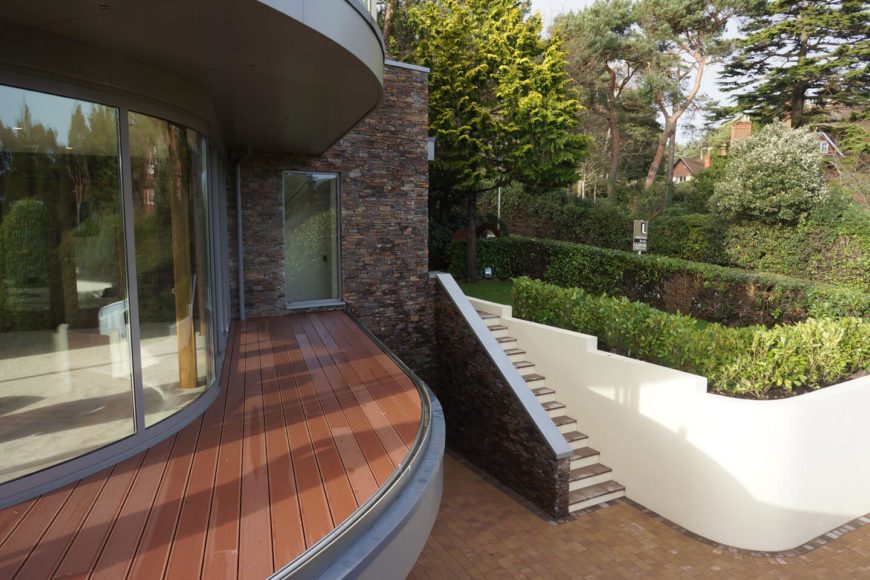 Above the garage, we see the rich hardwood deck cladding on the first balcony, here before the glass railing wall was installed. The brick structure stands as the root of the building. Above the garage, we see the rich hardwood deck cladding on the first balcony, here before the glass railing wall was installed. The brick structure stands as the root of the building.