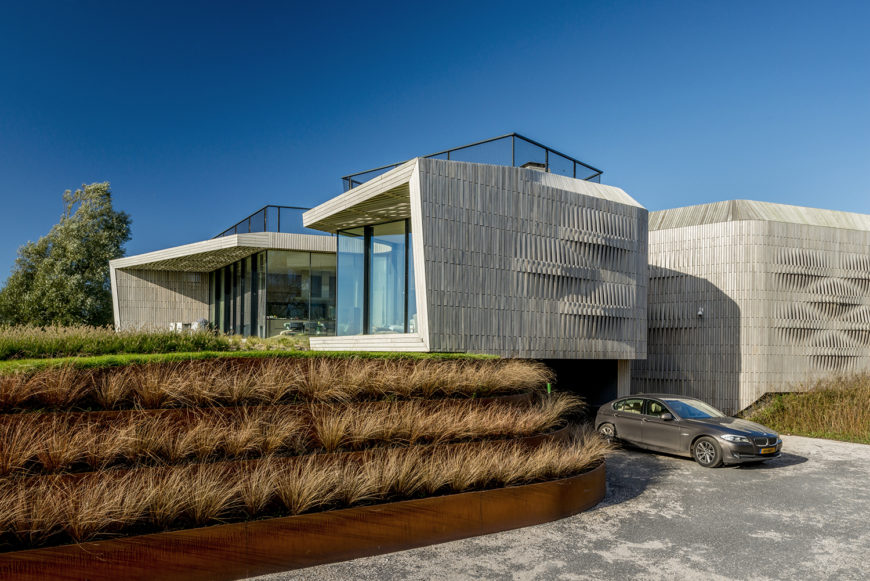 The home's garage is tucked beneath one of the four wings of the house, below the main floor. The driveway is rimmed by terraces of grasses that lead up to the lush green yard. The home's garage is tucked beneath one of the four wings of the house, below the main floor. The driveway is rimmed by terraces of grasses that lead up to the lush green yard.