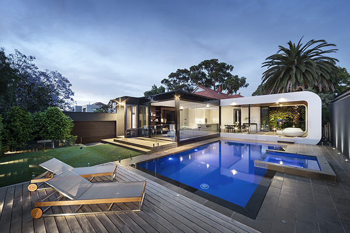 The back of the home consists of unique glazing, exposing the kitchen, living room, dining room, and 3-seasons room. The landscaping mimicks the modern design from the backside of the house, and pulls it into the patio– modernizing the outside with grey concrete and a brilliant blue pool. The back of the home consists of unique glazing, exposing the kitchen, living room, dining room, and 3-seasons room. The landscaping mimicks the modern design from the backside of the house, and pulls it into the patio– modernizing the outside with grey concrete and a brilliant blue pool.