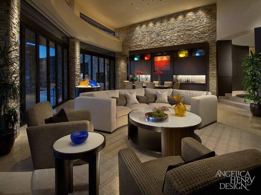 In a luxurious contemporary home, the stone walls are interrupted by a large wall with a built-in dark wood bar. The simple design of the bar also conceals lighted display cases and a beautiful painting that would be lost on the textured stone walls.