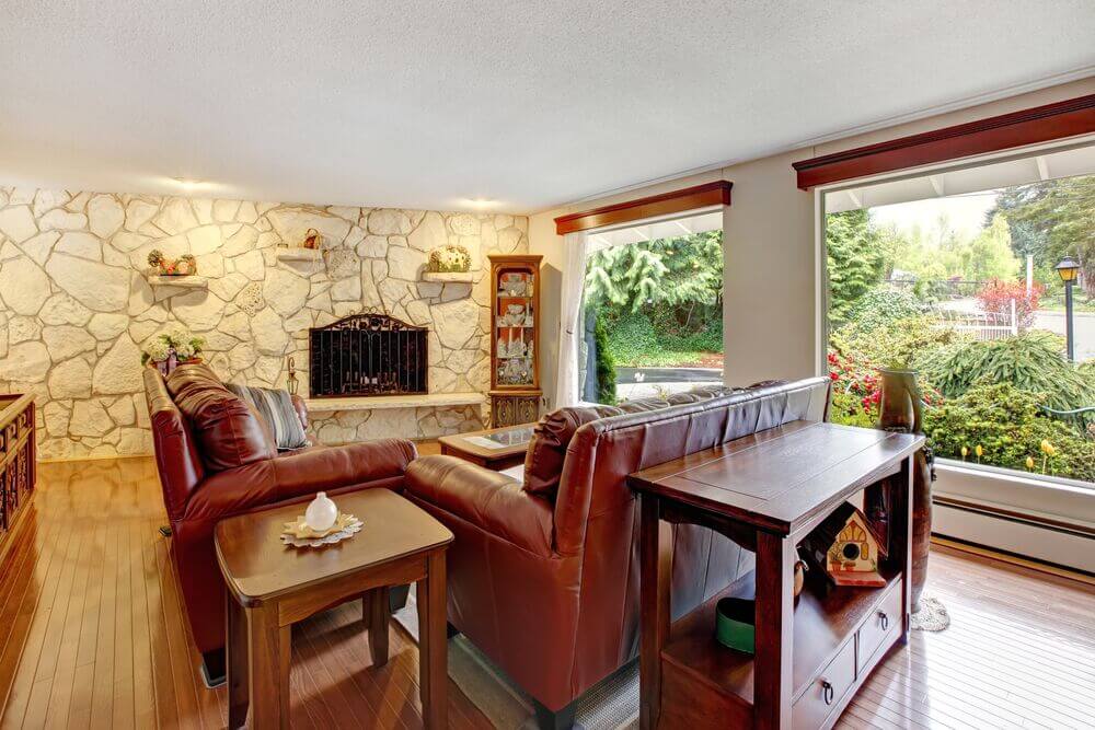 A long stone wall on one side of this light and bright living room draws the eye away from the huge seamless windows and to the mostly unadorned fireplace.