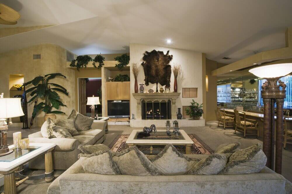 This ornate and luxurious living room and bar is filled with tall, textured beige walls, except for the white wall with the fireplace. The white allows the fireplace and fur wall decor to stand out.