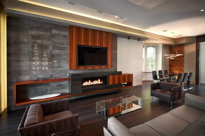 This highly modernized living room features sleek leather chairs and a sofa along with wooden accents and shelving with a heavy wood grain. The wall behind the entertainment center is in a beautiful dark stone tile, which acts as a contrast to the light neutrals on the other walls.
