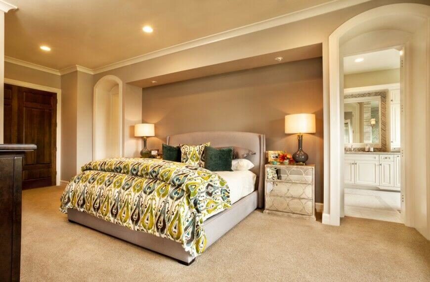 This gorgeous bedroom has a large bed in the center of the room. This fabric headboard is a neutral taupe color, and contrasts with the playful patterned green comforter and pillows. This gorgeous bedroom has a large bed in the center of the room. This fabric headboard is a neutral taupe color, and contrasts with the playful patterned green comforter and pillows.