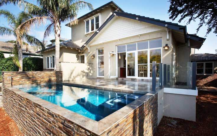 An exterior shot of the rear of the home reveals a tile patio leading out to a small and unique turquoise blue pool encased in earth-tone brick. Gorgeous windows allow a peek into the dining area, and allow for plenty of natural light to diffuse throughout the home. An exterior shot of the rear of the home reveals a tile patio leading out to a small and unique turquoise blue pool encased in earth-tone brick. Gorgeous windows allow a peek into the dining area, and allow for plenty of natural light to diffuse throughout the home.