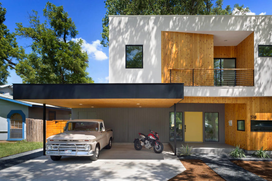 The upper level features a uniquely shaped balcony, cut within the external structure itself and flush with natural wood. The lower level entry area is clad in grey, highlighted by a soft yellow hued door. The upper level features a uniquely shaped balcony, cut within the external structure itself and flush with natural wood. The lower level entry area is clad in grey, highlighted by a soft yellow hued door.
