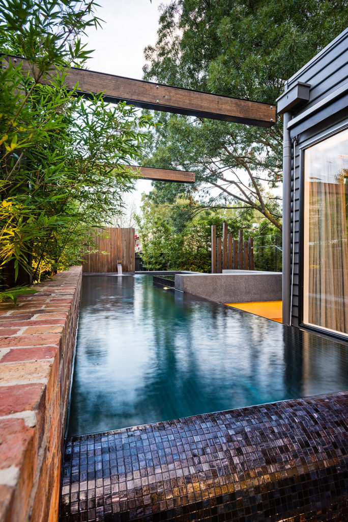 A closer look at the pool reveals the recycled brick edging that supports a row of wraparound bamboo plants in lieu of a traditional fencing solution. The black steel and timber arbors loom overhead to striking effect. A closer look at the pool reveals the recycled brick edging that supports a row of wraparound bamboo plants in lieu of a traditional fencing solution. The black steel and timber arbors loom overhead to striking effect.