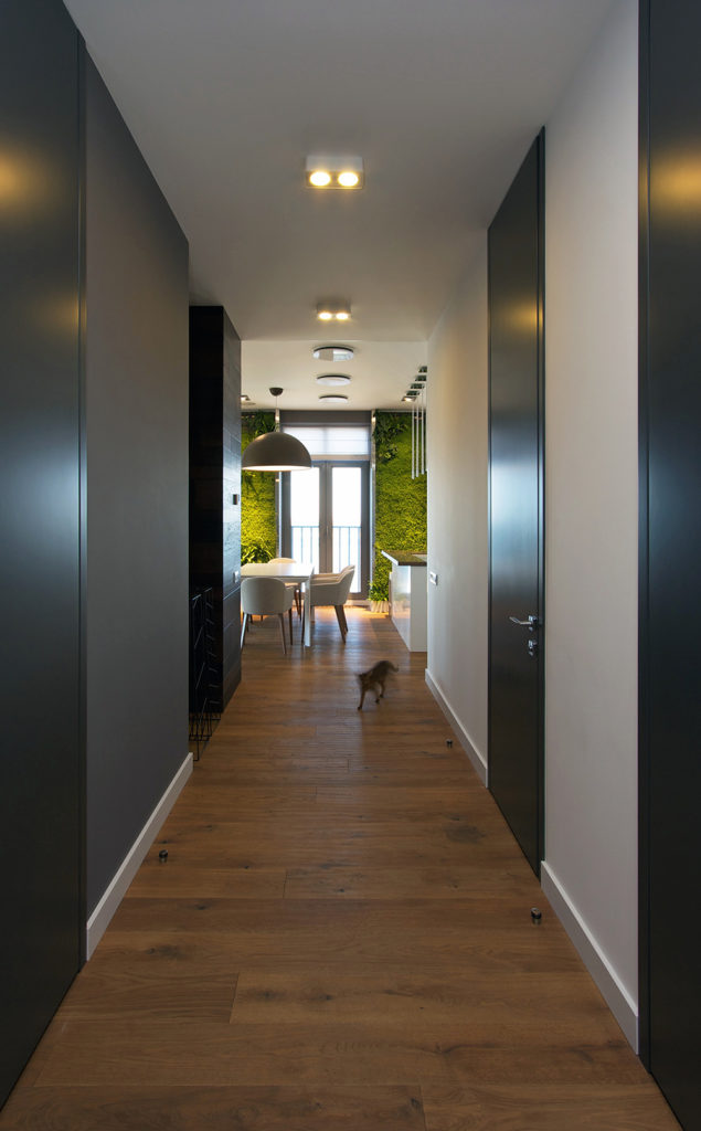 As we continue along the length of the hallway, we see the opening into the main living area of the home. Opposite sides of the hall are painted in different shades of gray, which contrast and complement the matte black doors. As we continue along the length of the hallway, we see the opening into the main living area of the home. Opposite sides of the hall are painted in different shades of gray, which contrast and complement the matte black doors.