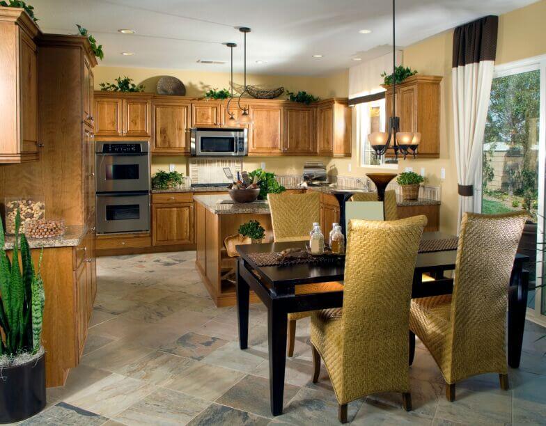 In a more contemporary setting, this kitchen features lush natural wood cabinetry over stone tile flooring. The black stained dining table is flanked by high-back wicker upholstered chairs for bold contrast. In a more contemporary setting, this kitchen features lush natural wood cabinetry over stone tile flooring. The black stained dining table is flanked by high-back wicker upholstered chairs for bold contrast.