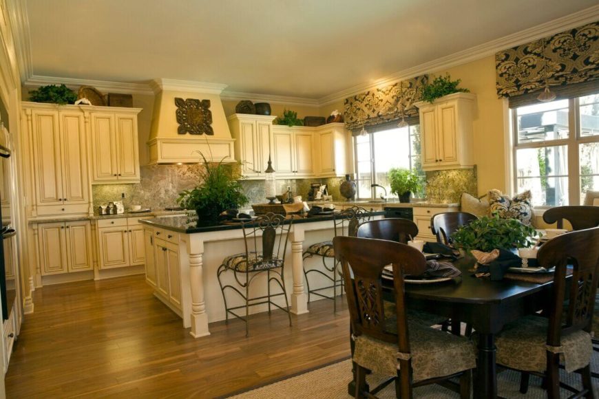 The ornate cabinetry and island design in this kitchen makes it truly stand out as a detail-rich environment. The dark wood dining table brings contrast and utility to this large room. The ornate cabinetry and island design in this kitchen makes it truly stand out as a detail-rich environment. The dark wood dining table brings contrast and utility to this large room.
