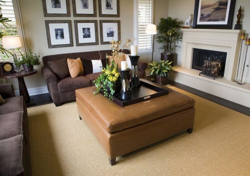 A much lighter brown ottoman doubles as a coffee table between two chocolate-brown velour sofas. To the right is an elevated wood-burning fireplace. A lighter brown ottoman allows for accent pillows in a matching shade to pull color to the darker sofas. A much lighter brown ottoman doubles as a coffee table between two chocolate-brown velour sofas. To the right is an elevated wood-burning fireplace. A lighter brown ottoman allows for accent pillows in a matching shade to pull color to the darker sofas.