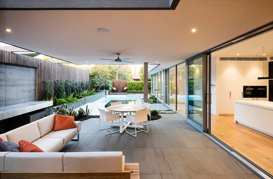 The seating area is covered by a roof supported by posts and opens up into the kitchen of the house by way of a large sliding door. The charcoal planter along the left side extends the entire length of the property and is filled with a carefully chosen selection of plants with a ficus hedge. The plants are backed by horizontal screen boards along the boundary of the property, creating a striking contrast. The seating area is covered by a roof supported by posts and opens up into the kitchen of the house by way of a large sliding door. The charcoal planter along the left side extends the entire length of the property and is filled with a carefully chosen selection of plants with a ficus hedge. The plants are backed by horizontal screen boards along the boundary of the property, creating a striking contrast.