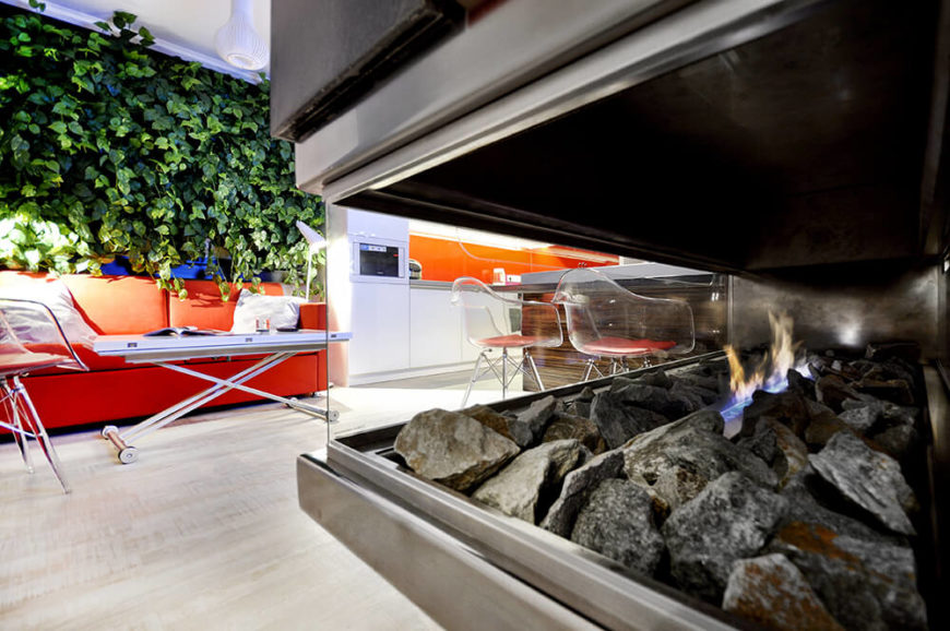 Here's a look through the floating fireplace at the open living room and kitchen area. The bright patches of orange truly jump out immediately, setting the stage for the whole space. Here's a look through the floating fireplace at the open living room and kitchen area. The bright patches of orange truly jump out immediately, setting the stage for the whole space.