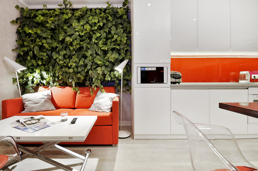 Glossy white cabinetry stands at great contrast to the lush wall garden, emphasizing the sharp mood of the home. An orange sofa matches the sleek backsplash seen at right. Glossy white cabinetry stands at great contrast to the lush wall garden, emphasizing the sharp mood of the home. An orange sofa matches the sleek backsplash seen at right.