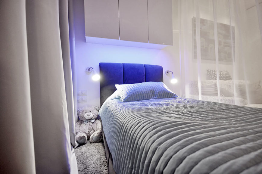 The bed features a soft blue headrest flanked by a pair of articulated sconces. Above is a set of sleek white cabinetry. To the left, we can see all of the lighting controls, mounted within reach of anyone in the bed. The bed features a soft blue headrest flanked by a pair of articulated sconces. Above is a set of sleek white cabinetry. To the left, we can see all of the lighting controls, mounted within reach of anyone in the bed.