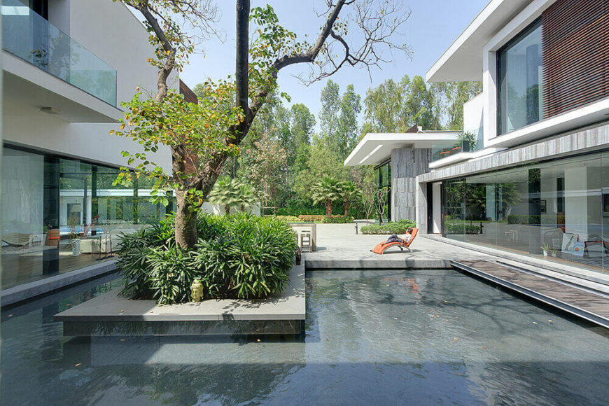 The courtyard features an intricate dance of natural and man made elements, most notably evoked in this wraparound reflection pool and the large tree at center. On both sides, rooms within the home can be seen through full height glass. The courtyard features an intricate dance of natural and man made elements, most notably evoked in this wraparound reflection pool and the large tree at center. On both sides, rooms within the home can be seen through full height glass.
