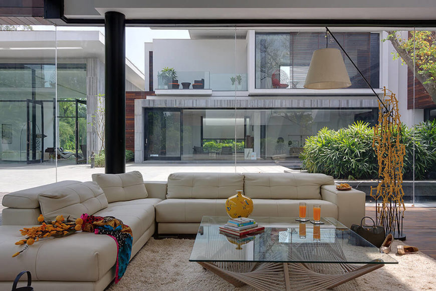 The living room is filled with lush modern furniture and intricate works of art, like the floor lamp sculpture in yellow. The structure of the home is revealed as a series of open box designs in the background. The living room is filled with lush modern furniture and intricate works of art, like the floor lamp sculpture in yellow. The structure of the home is revealed as a series of open box designs in the background.