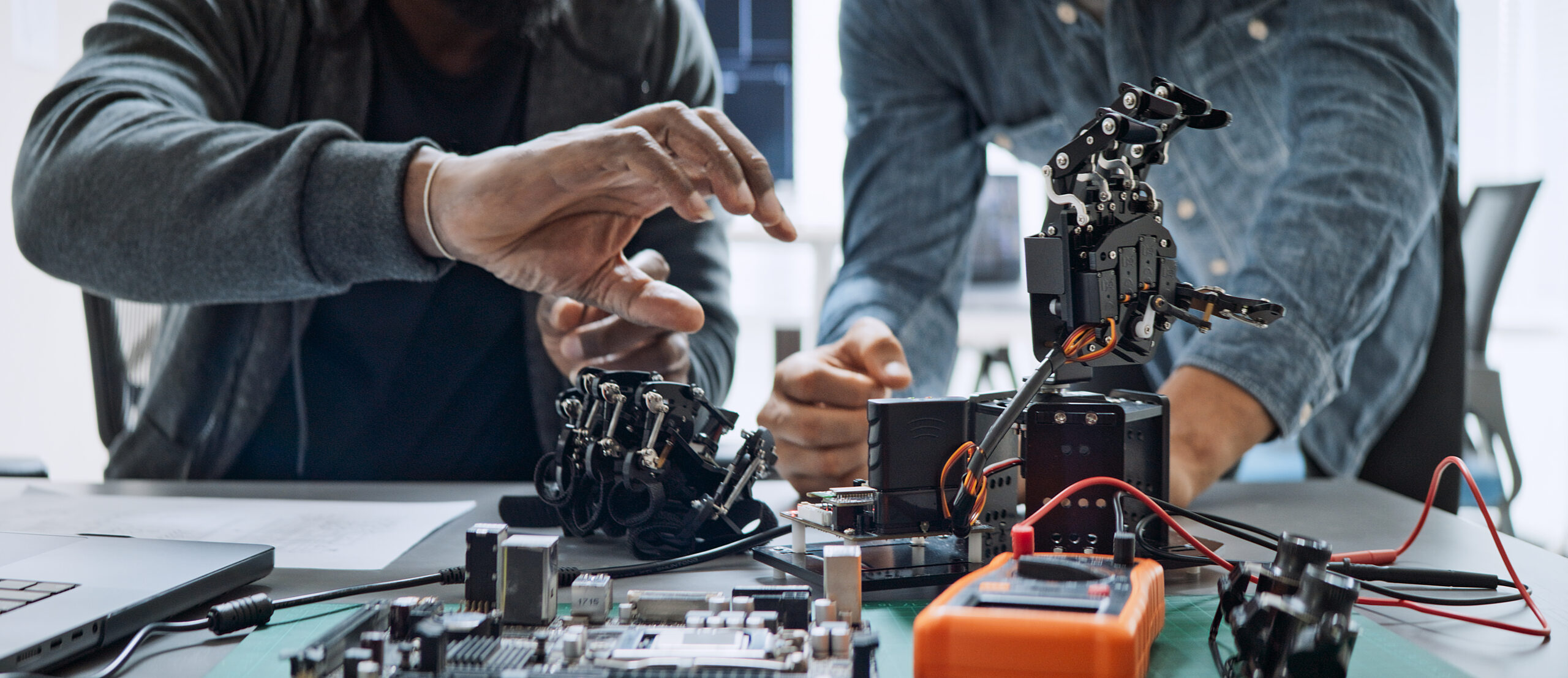 Black and white male software developer programmers work together on robot hand machine coding, use computer control robotic arm circuit. Programming language, hardware development technology concept