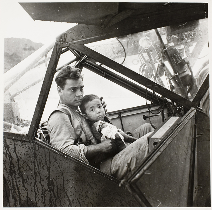 [American soldier tenderly holding a wounded Japanese boy inside an airplane as they await a flight to the nearest field hospital]