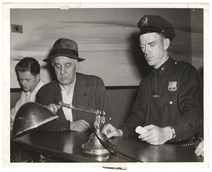 [Police officer who looks like Gary Cooper booking blind man for muder, New York]