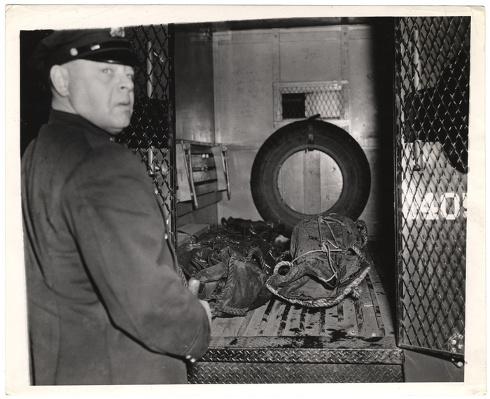 [Police officer and wrapped objects in the back of a police truck]