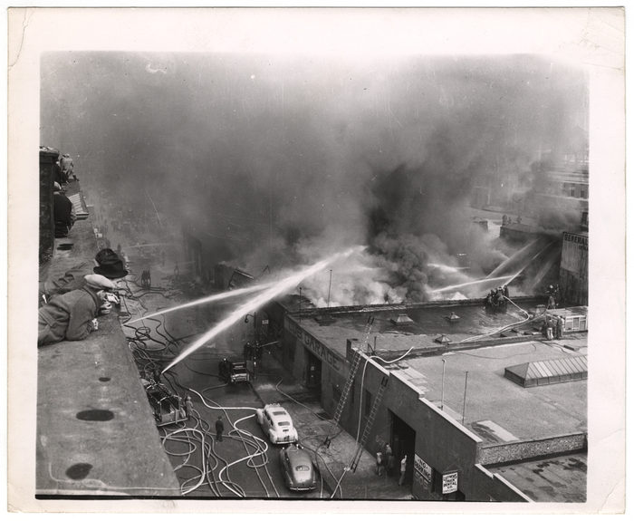 Rooftop watchers see 55th St. garage burn to ground. Gasoline tank expolsions prevented saving of trucks stored inside