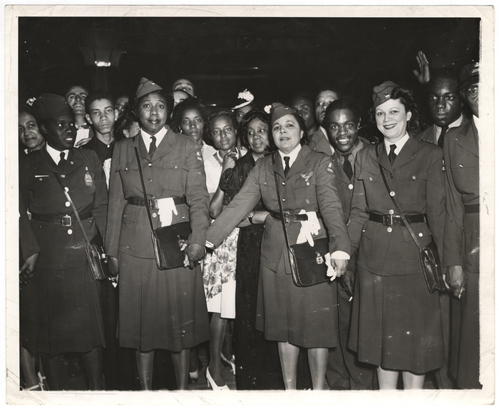 [Women wearing military uniforms holding hands]